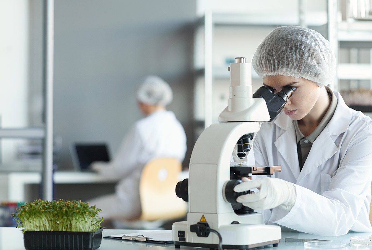portrait-young-female-scientist-looking-microscope-while-studying-plant-samples-biotechnology-lab-copy-space