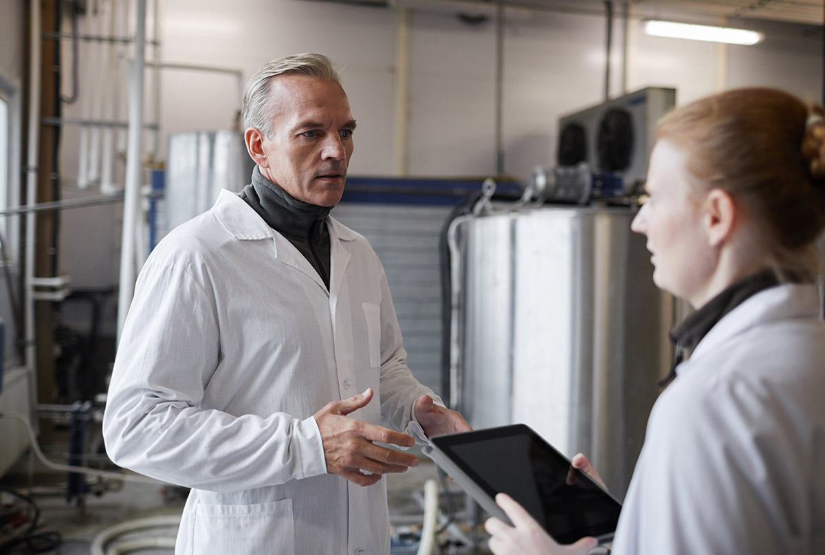 waist-up-portrait-mature-man-instructing-female-worker-while-discussing-work-food-production-factory-copy-space
